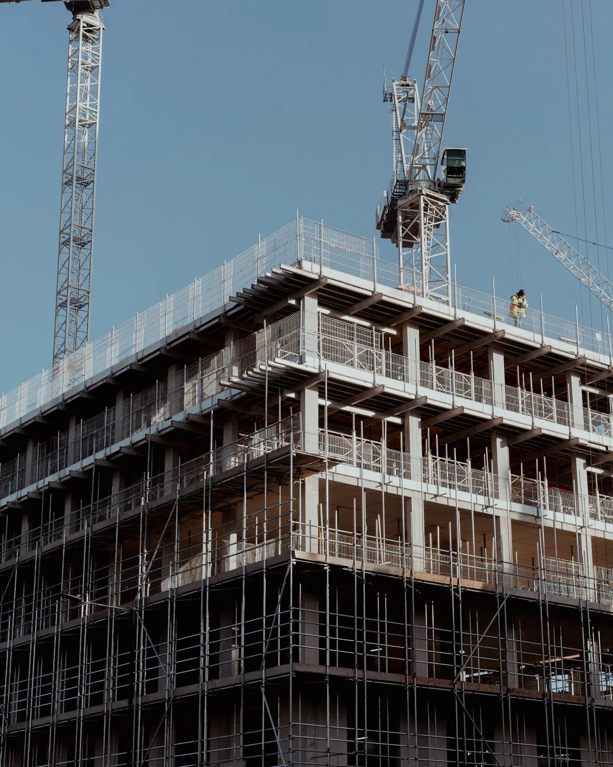 Scaffolded concrete building under construction with tower cranes
